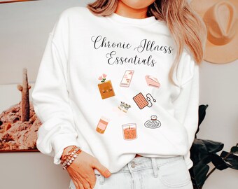 May include: White sweatshirt with the text "Chronic Illness Essentials" and illustrations of items like a book, phone, tea bag, candle, and pills.