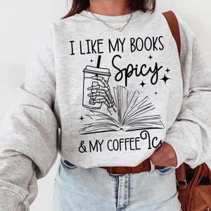 May include: A grey sweatshirt with the text "I like my books spicy & my coffee iced" and a graphic of a skeleton hand holding a cup of coffee and a book.