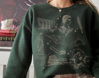 Op de afbeelding: Een donkergroen sweatshirt met een witte grafische print van Romeinse architectuur, wolken en een zon. De grafiek bevat ook een vrouw in een toga, een stapel boeken en een vrouw die een rol papier vasthoudt.
