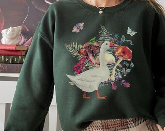 May include: A dark green sweatshirt with a white goose and mushroom print. The goose is surrounded by leaves, flowers, and butterflies.