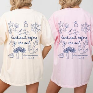 May include: Two white and pink t-shirts with a nautical theme. The shirts feature a graphic of an anchor, palm trees, seashells, a ring, and a ship's wheel. The text on the shirts reads "last sail before the veil" and "diviay bachelorette miami fl".