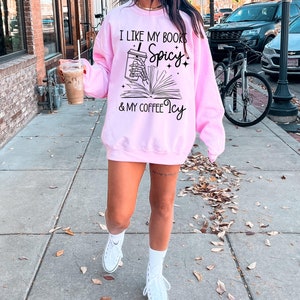May include: A pink sweatshirt with the text "I like my books Spicy & my coffee Icy" and a graphic of a book with a coffee cup on top of it.