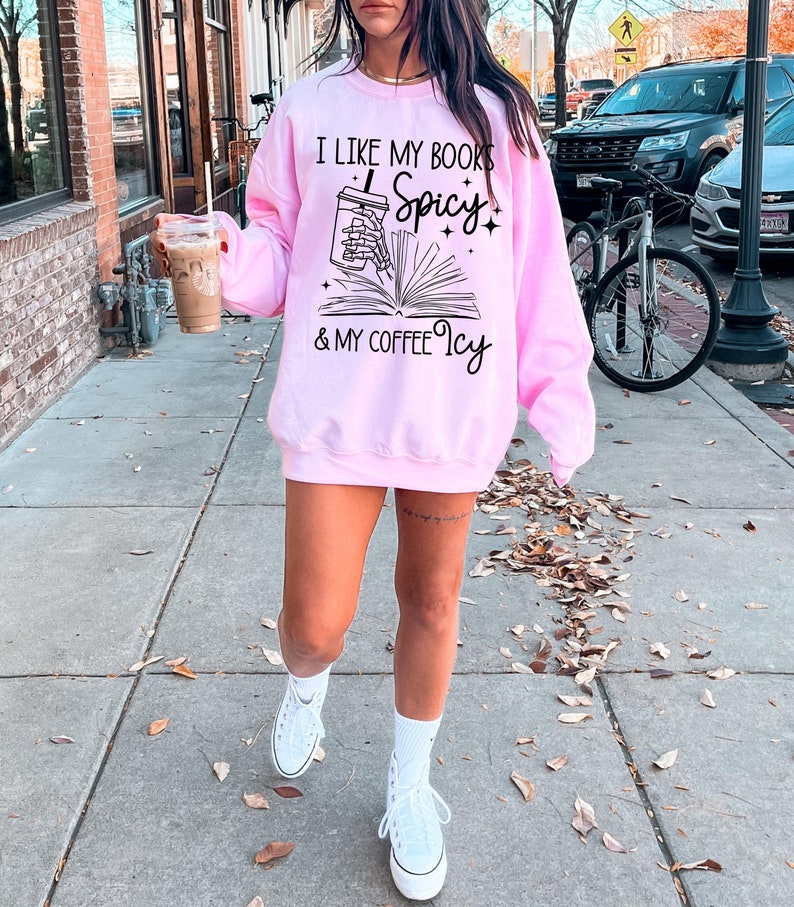 May include: A pink sweatshirt with the text "I like my books Spicy & my coffee Icy" and a graphic of a book with a coffee cup on top of it.