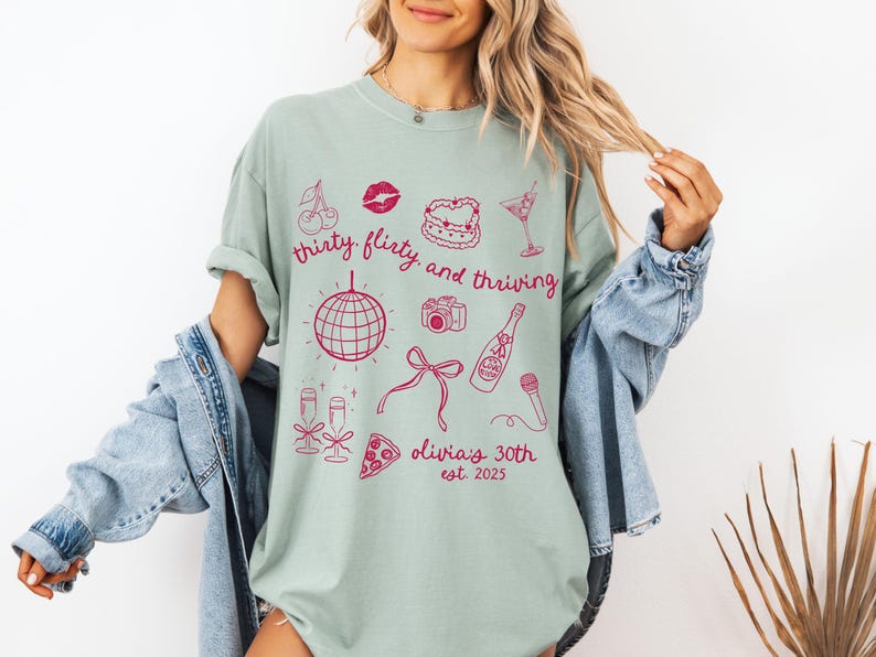 Może przedstawiać: Jasnozielony t-shirt z r&oacute;żowym nadrukiem graficznym przedstawiającym kulę dyskotekową, butelkę szampana, wiśnie, kawałek pizzy, aparat fotograficzny, szminkę, ciasto i kieliszek martini. Tekst na koszulce brzmi "thirty flirty and thriving Olivia's 30th est. 2025".