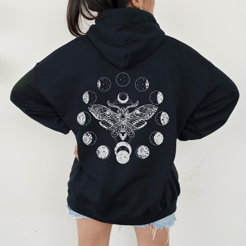 May include: Black hooded sweatshirt with a white graphic of a moth and phases of the moon. The moth design is centered on the back of the sweatshirt. The moon phases are arranged in a circle around the moth.