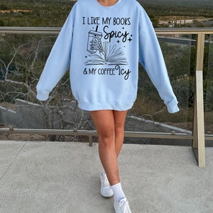May include: A light blue sweatshirt with the text "I like my books Spicy & my coffee Icy" and a graphic of a skeleton hand holding a coffee cup and a book.
