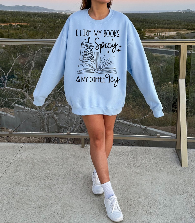 May include: A light blue sweatshirt with the text "I like my books Spicy & my coffee Icy" and a graphic of a skeleton hand holding a coffee cup and a book.