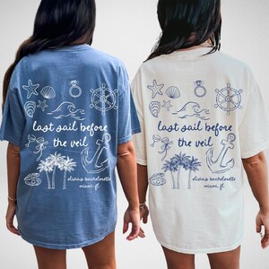 May include: Two light blue and white t-shirts with a nautical theme. The shirts have a graphic design with an anchor, palm trees, seashells, a ring, and a steering wheel. The text on the shirts reads "last sail before the veil" and "oliviay bachelorette miami fl".