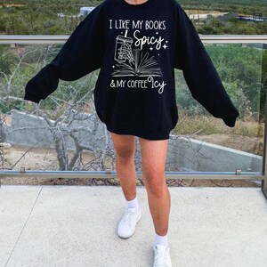May include: Black sweatshirt with a white graphic that says "I like my books spicy & my coffee icy". The graphic features a hand holding a cup of coffee and a book.