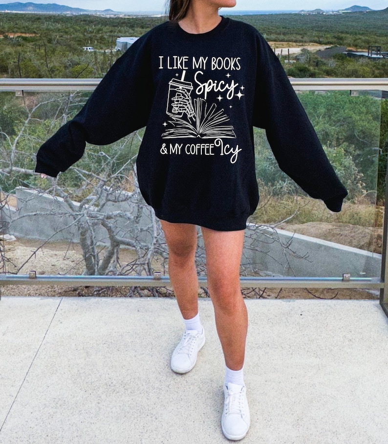 May include: Black sweatshirt with a white graphic that says "I like my books spicy & my coffee icy". The graphic features a hand holding a cup of coffee and a book.