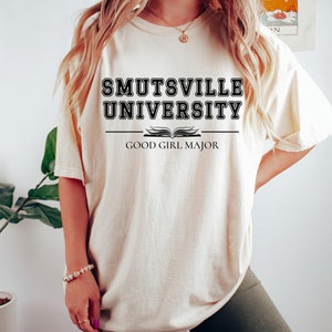 May include: An oversized white t-shirt with black text that reads "Smutsville University" with an open book graphic and the text "Good Girl Major" underneath.