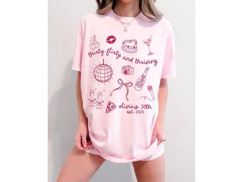 Może przedstawiać: R&oacute;żowa koszulka z nadrukiem graficznym, kt&oacute;ry głosi "thirty flirty and thriving" z r&oacute;żnymi ilustracjami, w tym dyskoteką, butelką szampana, kawałkiem pizzy i wiśniami. Tekst "Olivia's 30th est. 2025" jest r&oacute;wnież zawarty w projekcie.