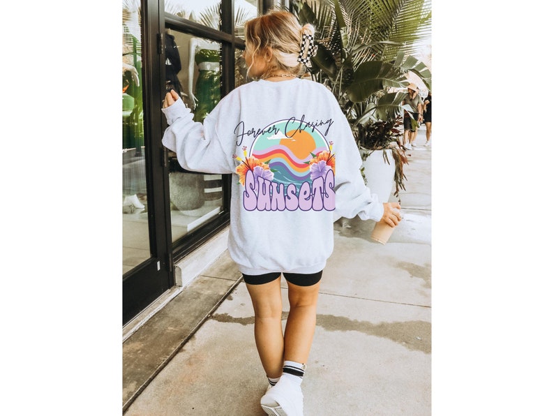 May include: White sweatshirt with a graphic print of a sunset with the text "Forever Chasing Sunsets" in purple and white.