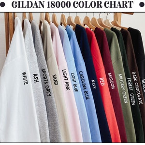 May include: Colour chart for Gildan 18000 t-shirts, displaying 14 different colours: black, dark chocolate, forest green, military green, maroon, red, navy, Carolina blue, light blue, light pink, sand, sports grey, ash, and white.