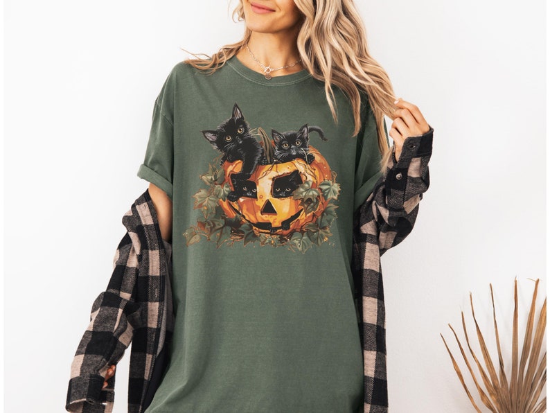 Peut inclure: Un t-shirt vert avec un motif de trois chatons noirs &agrave; l'int&eacute;rieur d'une citrouille. Les chatons regardent hors de la citrouille.