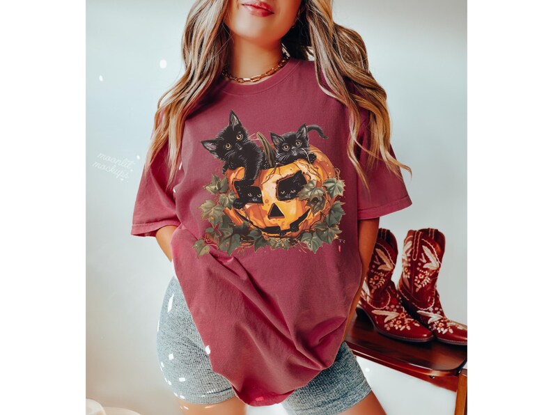 Peut inclure: Un t-shirt marron avec un motif de trois chatons noirs &agrave; l'int&eacute;rieur d'une citrouille d'Halloween. Les chatons regardent hors de la citrouille.