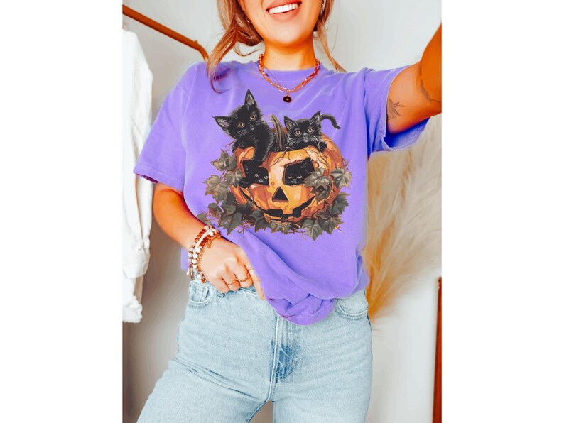 Peut inclure: Un t-shirt violet avec un motif de trois chatons noirs &agrave; l'int&eacute;rieur d'une citrouille. Les chatons regardent hors de la citrouille.