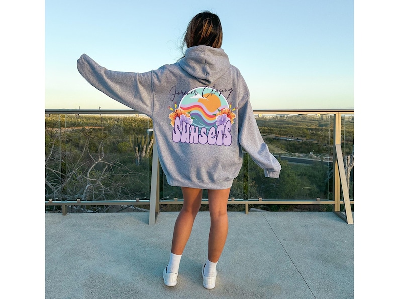 May include: A grey hooded sweatshirt with a graphic print on the back. The graphic features a colourful sunset with the text "Forever Chasing Sunsets".