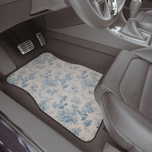 May include: A white car floor mat with a blue floral pattern. The mat is in the driver's side footwell of a car.