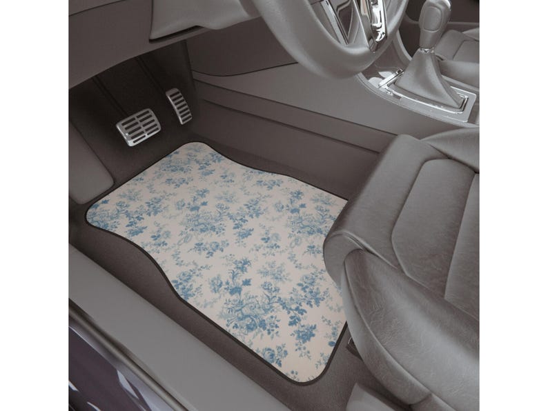 May include: A white car floor mat with a blue floral pattern. The mat is in the driver's side footwell of a car.