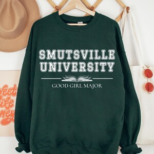 May include: A dark green sweatshirt with white text that reads "Smutsville University Good Girl Major".
