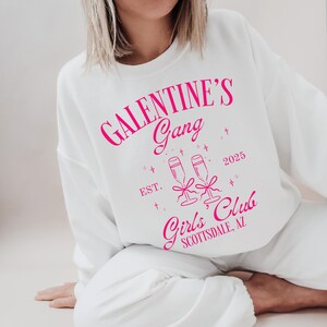 May include: White sweatshirt with pink text that reads "Galentine's Gang Est. 2025 Girls' Club Scottsdale, AZ" with a graphic of two champagne glasses.
