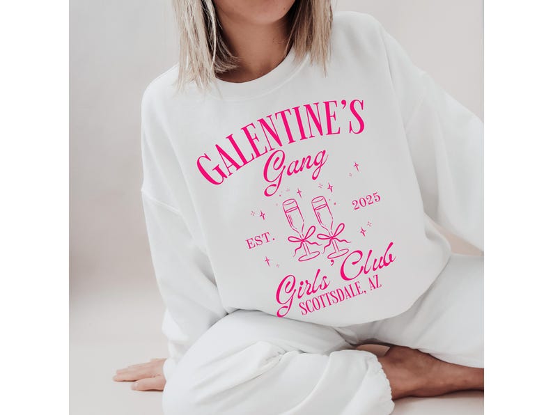 May include: White sweatshirt with pink text that reads "Galentine's Gang Est. 2025 Girls' Club Scottsdale, AZ" with a graphic of two champagne glasses.