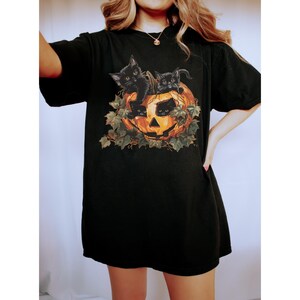 Peut inclure: T-shirt noir avec un motif de trois chatons noirs &agrave; l'int&eacute;rieur d'une citrouille d'Halloween.