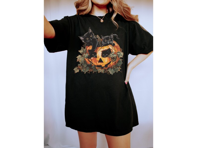 Peut inclure: T-shirt noir avec un motif de trois chatons noirs &agrave; l'int&eacute;rieur d'une citrouille d'Halloween.