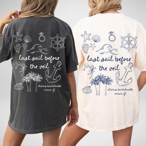 May include: Two white t-shirts with a nautical theme. The shirts have a graphic of an anchor, palm trees, seashells, a steering wheel, and the text "last sail before the veil". The text "Olivia's bachelorette Miami FL" is also on the shirts.