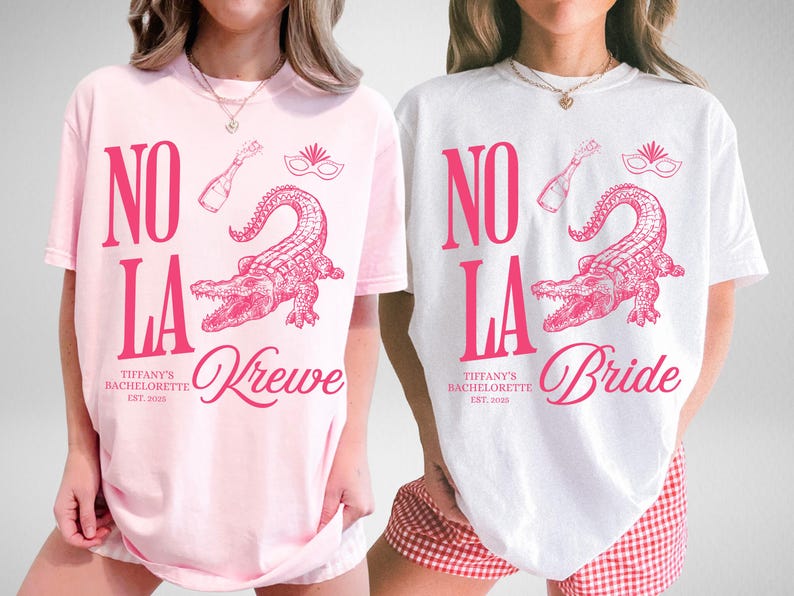 May include: Two t-shirts, one pink and one white, with a pink graphic design. The design includes the words "NO LA", an alligator, a champagne bottle, and a mask. The pink shirt says "Krewe" and the white shirt says "Bride".