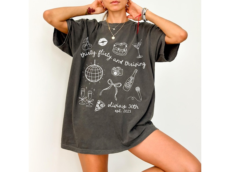 Może przedstawiać: Duży, ciemnoszary T-shirt z białym nadrukiem graficznym, kt&oacute;ry głosi "thirty flirty and thriving" i zawiera r&oacute;żne ikony związane z celebrowaniem, takie jak kula dyskotekowa, kieliszki do szampana, kawałek pizzy, aparat fotograficzny, butelka szampana, wiśnia, ciasto i kieliszek martini. W projekcie znajduje się r&oacute;wnież tekst "olivias 30th est. 2025".