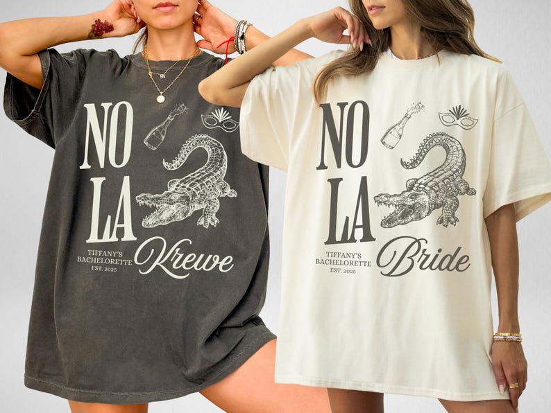 Two oversized t-shirts, one pepper and one ivory, featuring a graphic design. The design includes the text "NO LA", an alligator, a champagne bottle, and the text "Tiffany's Bachelorette Est. 2025" and "Krewe" or "Bride".
