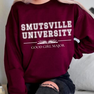 May include: Burgundy sweatshirt with white text that reads "Smutsville University" and "Good Girl Major" with an open book graphic.