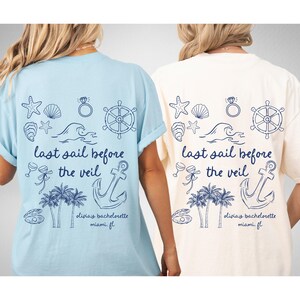May include: Two light blue and white t-shirts with a nautical theme. The shirts feature a variety of nautical icons, including an anchor, a steering wheel, a seashell, a wave, and a palm tree. The text on the shirts reads "last sail before the veil" and "Olivia's bachelorette Miami, FL".