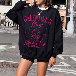 May include: Black sweatshirt with pink text that reads "Galentine's Gang Est. 2023 Girls' Club Scottsdale, AZ". The text is surrounded by a graphic of two champagne flutes.