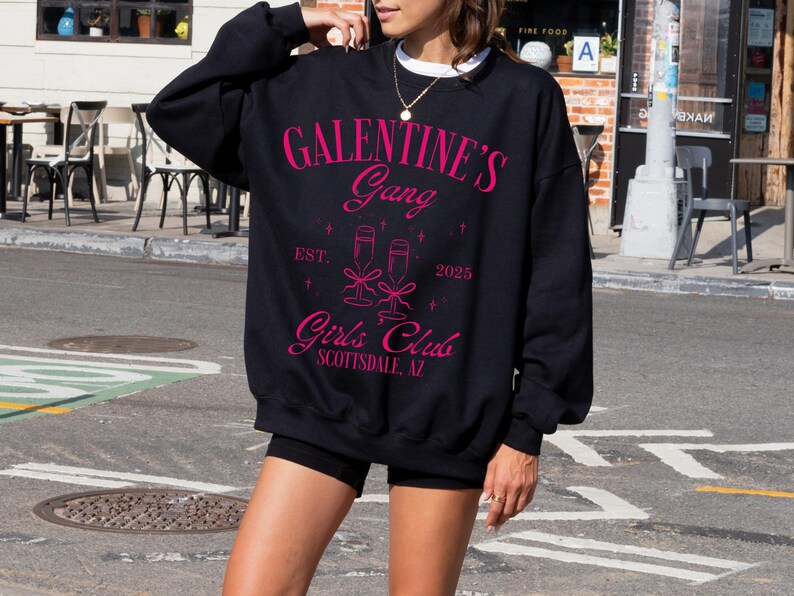 May include: Black sweatshirt with pink text that reads "Galentine's Gang Est. 2023 Girls' Club Scottsdale, AZ". The text is surrounded by a graphic of two champagne flutes.