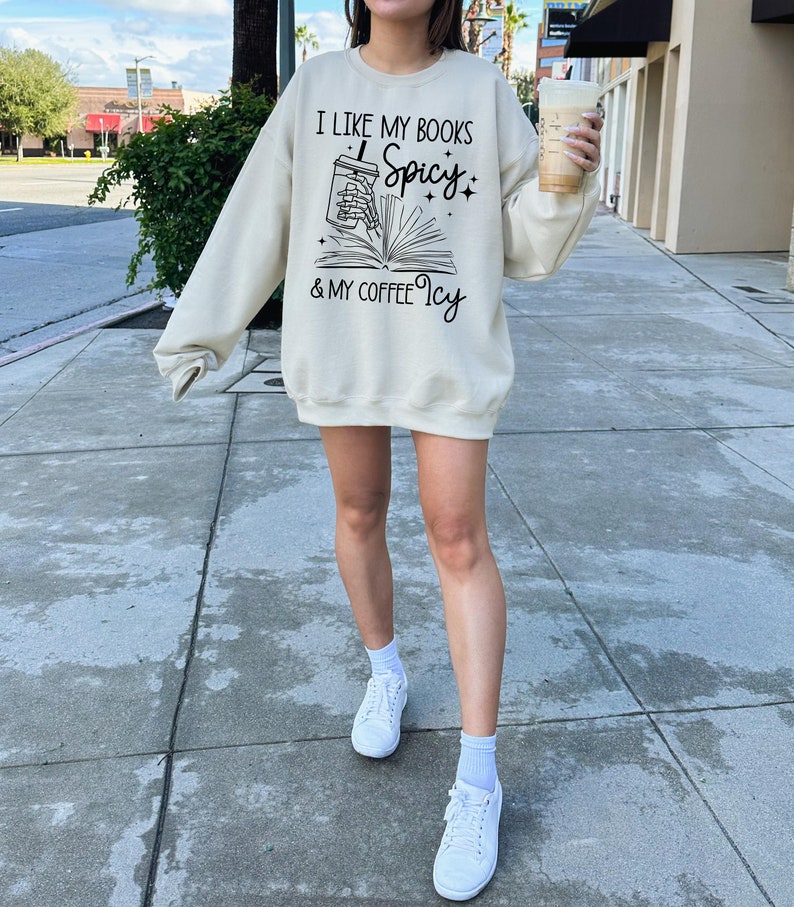 May include: A cream-coloured sweatshirt with a graphic print that says "I like my books spicy & my coffee icy". The graphic features a book with a coffee cup spilling out of it.