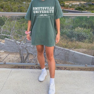 May include: A green t-shirt with the text "Smutsville University" and "Good Girl Major" printed on the front.