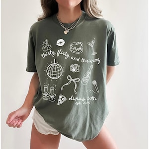 Może przedstawiać: Zielony T-shirt z białym tekstem, kt&oacute;ry brzmi "thirty flirty and thriving" i zawiera r&oacute;żne ilustracje związane z imprezą, w tym kulę dyskotekową, kieliszki do szampana, kawałek pizzy, aparat fotograficzny, kokardkę i mikrofon. Tekst na dole brzmi "Olivia's 30th est. 2023".