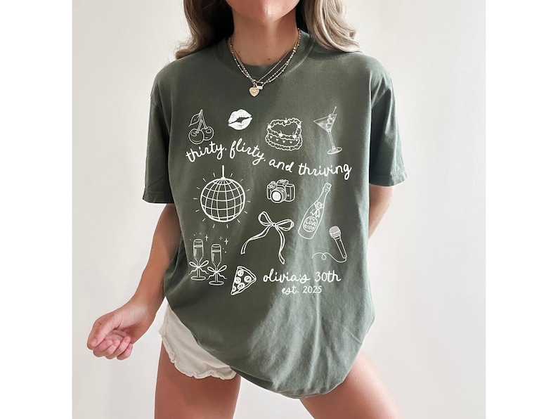 Może przedstawiać: Zielony T-shirt z białym tekstem, kt&oacute;ry brzmi "thirty flirty and thriving" i zawiera r&oacute;żne ilustracje związane z imprezą, w tym kulę dyskotekową, kieliszki do szampana, kawałek pizzy, aparat fotograficzny, kokardkę i mikrofon. Tekst na dole brzmi "Olivia's 30th est. 2023".