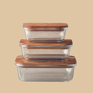 May include: Three glass storage containers with wooden lids. The containers are stacked on top of each other. The lids are made of natural wood.
