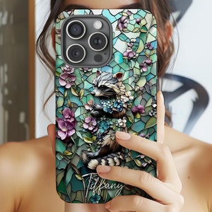 May include: A phone case with a stained glass design featuring a raccoon surrounded by flowers. The case has a personalized name, "Tiffany", printed on the bottom.