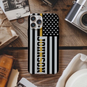 May include: A black and white American flag phone case with a yellow stripe and the name "JOHNSON" printed vertically on the stripe.