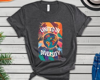 以下が含まれることがあります： 地球を囲むカラフルな手のグラフィックが描かれたダークグレーのTシャツ。グラフィックには「United in Diversity」と書いてあります。