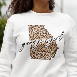 May include: White sweatshirt with a leopard print outline of the state of Georgia and the text "georgia girl" in black script.