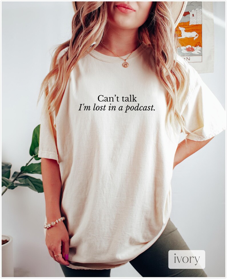 May include: A cream colored t-shirt with the text "Can't talk I'm lost in a podcast." printed in black.