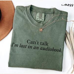 May include: A green t-shirt with the text "Can't talk I'm lost in an audiobook." printed in black.