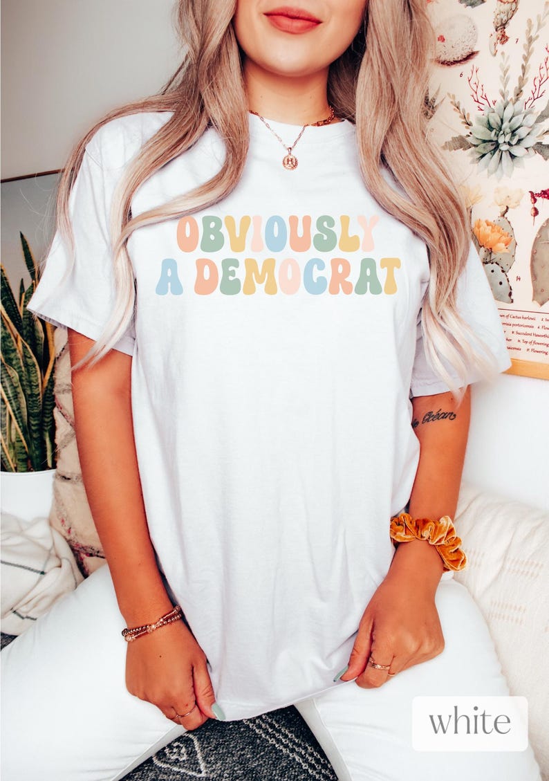 Puede incluir: Camiseta blanca con el texto "OBVIOUSLY A DEMOCRAT" en letras redondas y de colores.