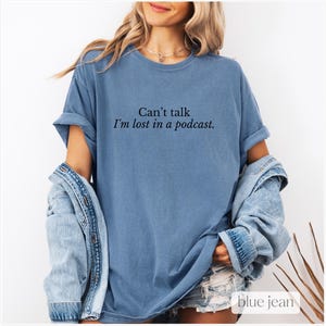 May include: A blue t-shirt with the text "Can't talk I'm lost in a podcast."